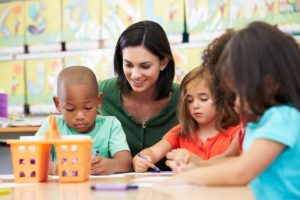 Group of Children In Art Class With Teacher Sitting Down At Table. Childcare.